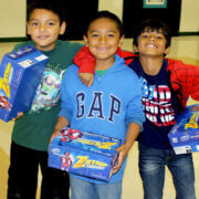 Three elementary aged friends all holding boxes with new shoes in them smiling