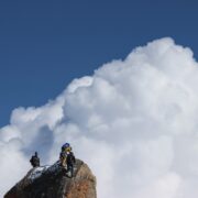 Three hikers scaling the peak of a large mountain to enjoy the view of clouds in the sky