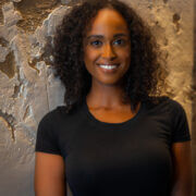 Nardos Alemayehu standing in front of a stone wall smiling with shoulder length black curly hair