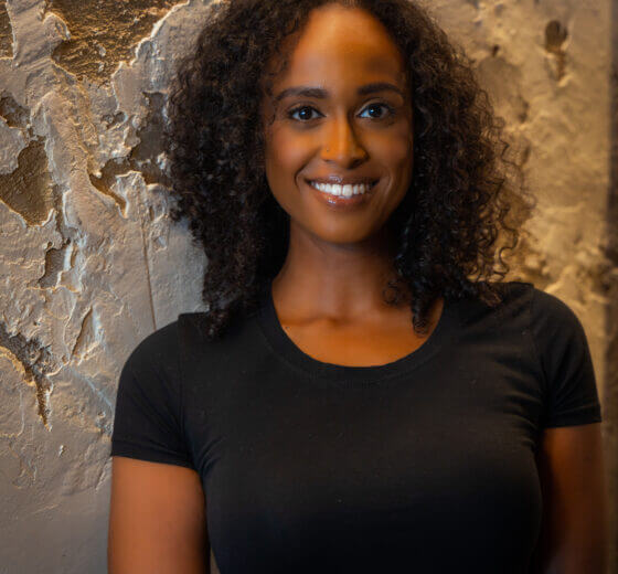 Nardos Alemayehu standing in front of a stone wall smiling with shoulder length black curly hair