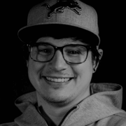 Smiling black and white photo of Nolan Marketti, who is wearing a Detroit Lions baseball cap, black glasses, and a zip up hoodie