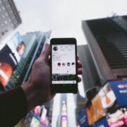 Zoomed out photo of hand holding iphone on instagram profile page. background is blurred with skyscrapers.