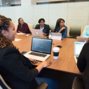A diverse group of professionals working together on their laptops around a large conference room table