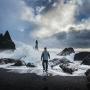 Man standing at the edge of a stormy ocean looking out on the rocky coast.
